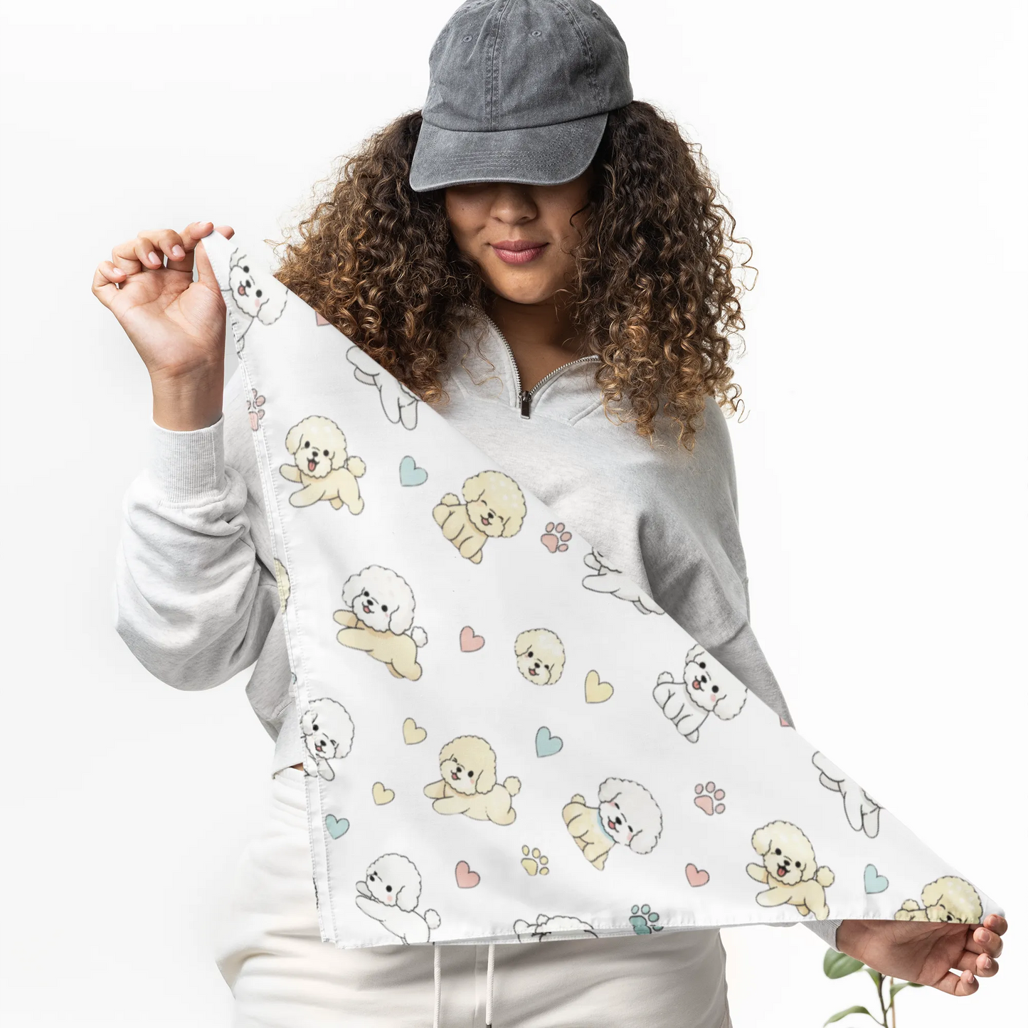 Woman holding a triangular cream bandana decorated with cute Bichon Frise dogs, pastel hearts and paw prints – stylish dog lover accessory mockup.