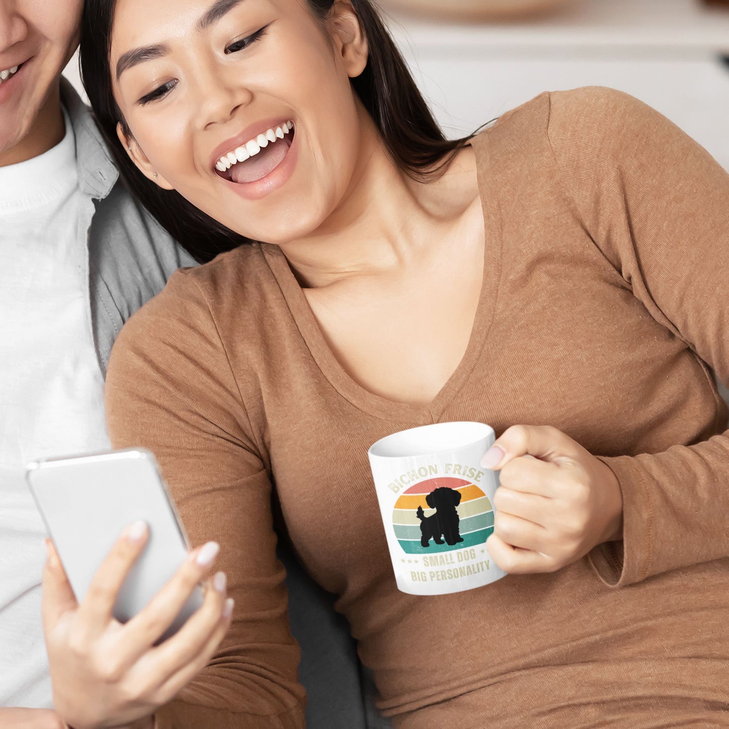 Smiling couple sitting on a sofa while the woman holds a white ceramic mug with retro Bichon Frise design and the text Small Dog Big Personality