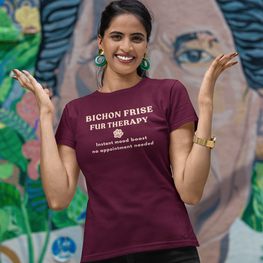 Smiling woman wearing a burgundy Bichon Frise Fur Therapy t-shirt with ‘Instant Mood Boost, No Appointment Needed’ slogan, casual outdoor setting with colorful mural background.