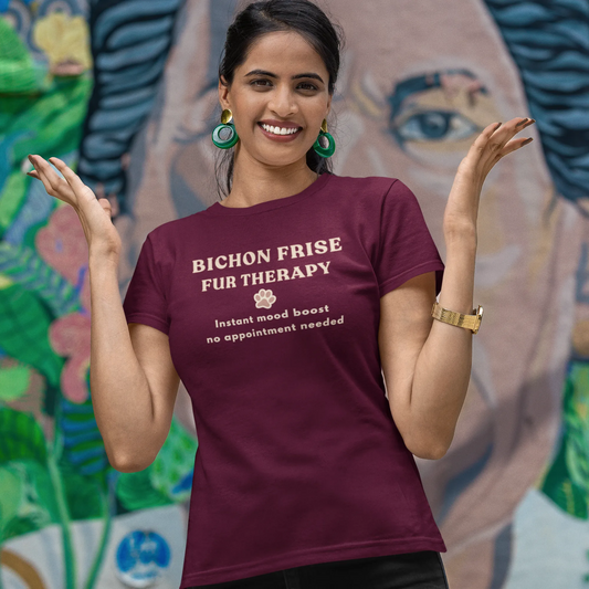 Smiling woman wearing a burgundy Bichon Frise Fur Therapy t-shirt with ‘Instant Mood Boost, No Appointment Needed’ slogan, casual outdoor setting with colorful mural background.