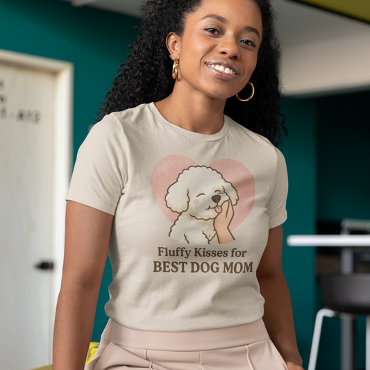 Smiling woman wearing a beige “Fluffy Kisses for the Best Dog Mom” Bichon Frise t-shirt, sitting indoors in a modern room – perfect for proud dog moms