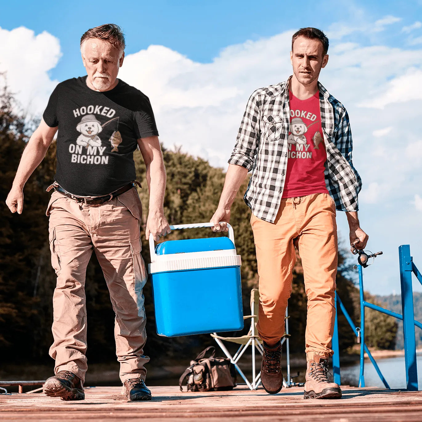 Two men walking on a dock near a lake wearing ‘Hooked on My Bichon’ funny fishing dog dad t-shirts, carrying a cooler and fishing gear, outdoor nature setting