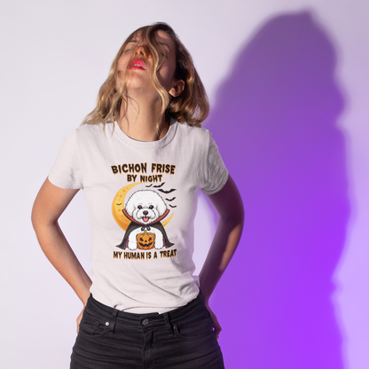 Woman wearing a white T-shirt with a Halloween-themed design of a Bichon Frise dressed as a vampire holding a pumpkin. The shirt text reads “Bichon Frise by Night – My Human Is a Treat”. Purple shadow background