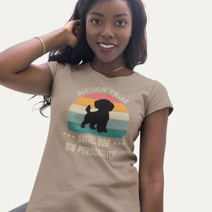 Woman wearing a retro-style beige T-shirt with 'Bichon Frise – Small Dog, Big Personality' design featuring a silhouette of a Bichon Frise in front of a vintage sunset graphic.