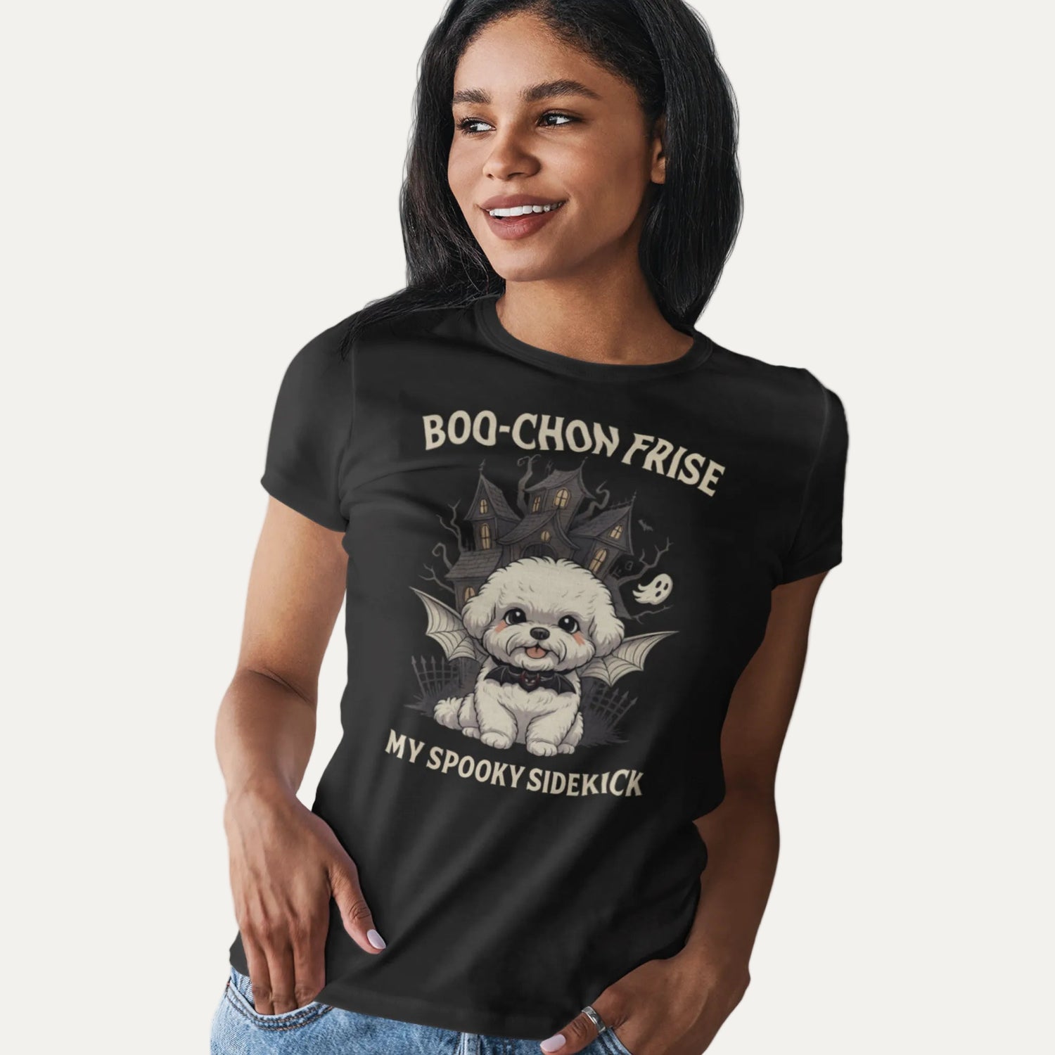 Woman wearing a black T-shirt featuring a cute Bichon Frise in a Halloween design with haunted house and ghost, labeled 'Boo-Chon Frise – My Spooky Sidekick