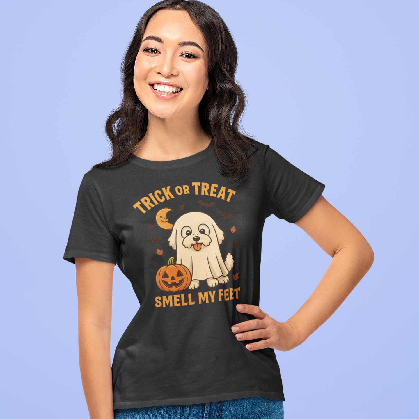 Smiling woman wearing a black Halloween t-shirt with a cute Bichon Frise dressed as a ghost and pumpkin, featuring the text 'Trick or Treat Smell My Feet'
